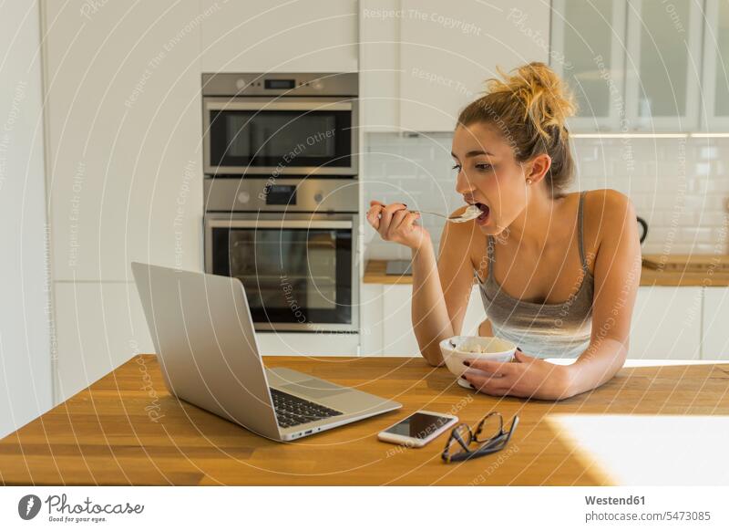 Weiblicher Teenager benutzt Laptop während des Frühstücks in der Küche Schale Schalen Schälchen Schüsseln Rechner Laptops Notebook Notebooks Telekommunikation