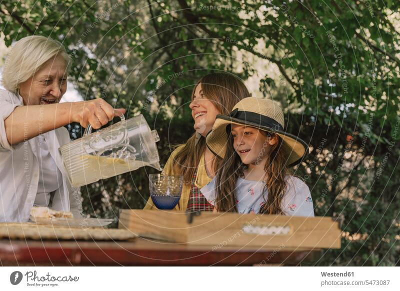 Ältere Frau schenkt im Hof Getränke für Tochter und Enkelin in Glas ein Farbaufnahme Farbe Farbfoto Farbphoto Spanien Freizeitbeschäftigung Muße Zeit Zeit haben