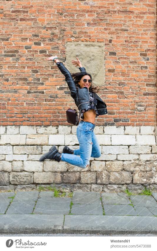 Junge Frau springt in die Luft, Backsteinmauer im Hintergrund Luftsprung Luftsprünge einen Luftsprung machen Luftspruenge unangepasst Unangepasstheit weiblich