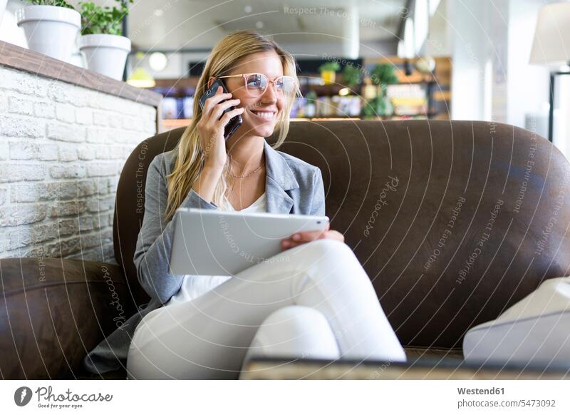 Junge Frau telefoniert mit ihrem Handy, während sie ihr digitales Tablet in einem Café benutzt geschäftlich Geschäftsleben Geschäftswelt Geschäftsperson