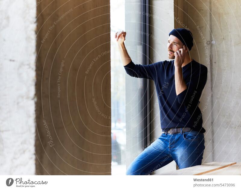 Junger Mann am Telefon schaut aus dem Fenster Deutschland nachdenken überlegen Beton zuhören zuhörend Drahtlose Technologie drahtlose Verbindung