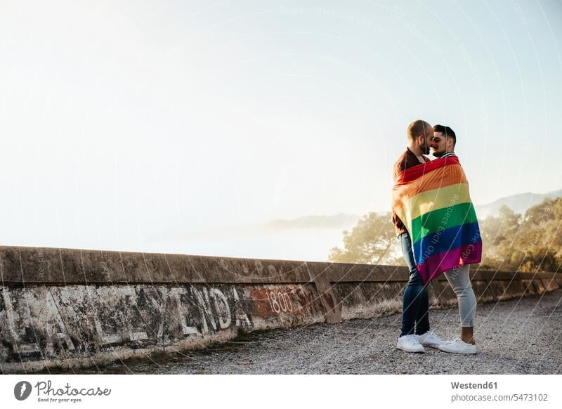 Homosexuelles Paar in einer Homosexuell Stolz Flagge eingewickelt küssen auf einer Straße in den Bergen Leute Menschen People Person Personen Europäisch
