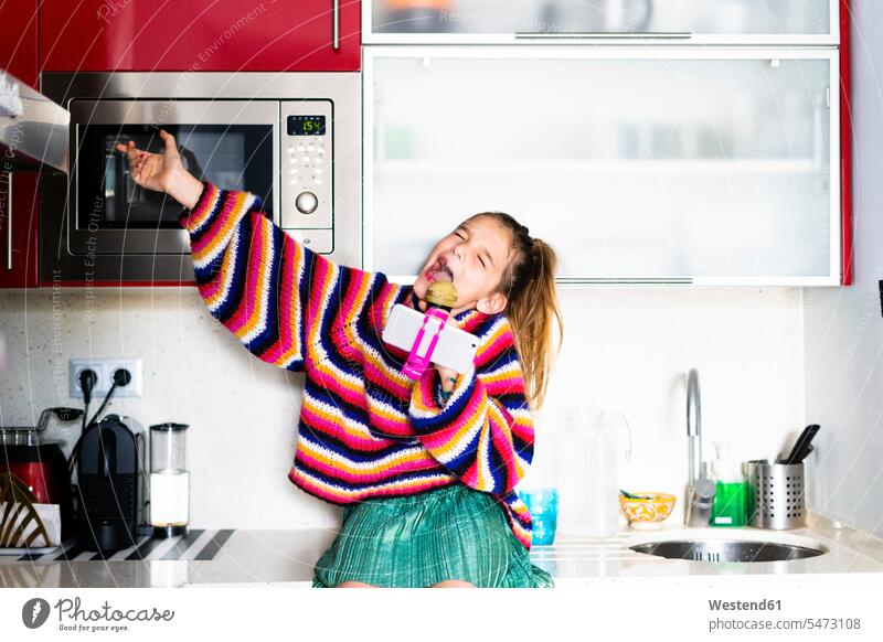 Mädchen spielt mit Mikrofon und Smartphone in der Küche zu Hause Zuhause daheim iPhone Smartphones spielen weiblich Mikrophone Mikrofone Handy Mobiltelefon