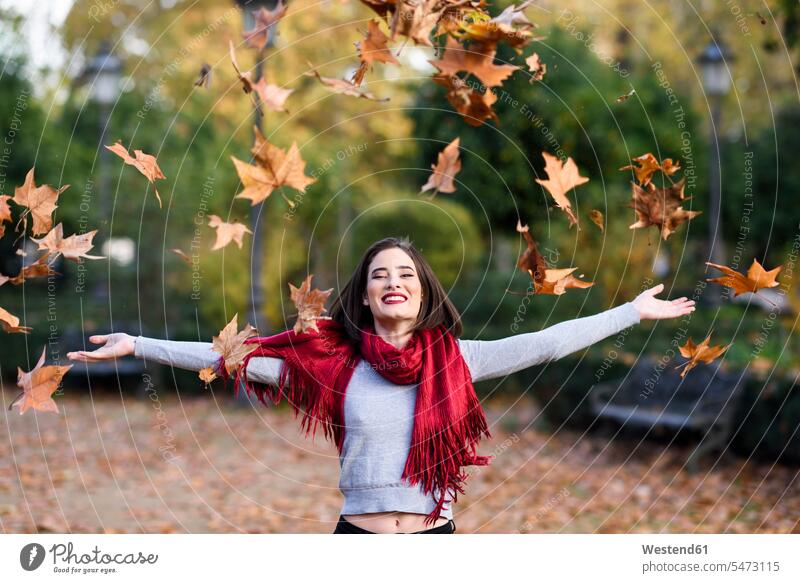 Porträt einer lachenden jungen Frau mit rotem Schal, die Herbstblätter in die Luft wirft Schals werfen Wurf weiblich Frauen Portrait Porträts Portraits roter