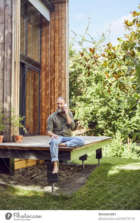 Bärtiger, reifer Mann spricht über Handy, während er vor einem winzigen Haus sitzt Farbaufnahme Farbe Farbfoto Farbphoto Deutschland Freizeitbeschäftigung Muße