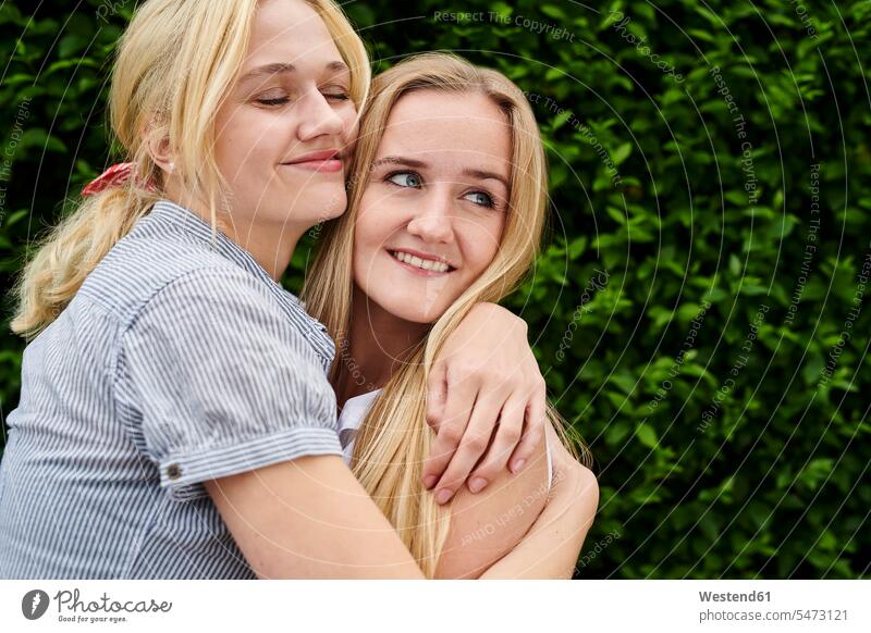 Zwei glückliche junge Frauen umarmen eine Hecke Umarmung Umarmungen Arm umlegen Hecken weiblich Freundinnen Glück glücklich sein glücklichsein Erwachsener