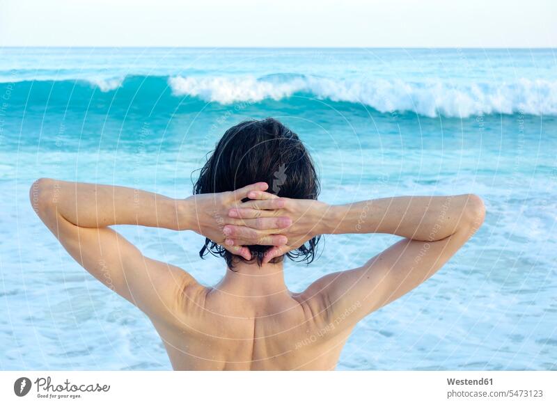 Seychellen, Rückenansicht eines Mannes mit Händen hinter dem Kopf vor dem Meer baden nackter Oberkörper freier Oberkörper Hand hinter dem Kopf