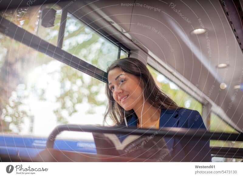 Junge Frau, die in einem Bus mit Kopfhörern Musik hört und aus dem Fenster schaut geschäftlich Geschäftsleben Geschäftswelt Geschäftsperson Geschäftspersonen