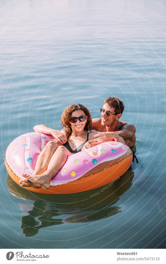 Glückliches junges Paar badet im Meer auf einem aufblasbaren Schwimmer in Donutform Touristen Badebekleidung Bikinis Luftmatratzen Brillen Sonnenbrillen