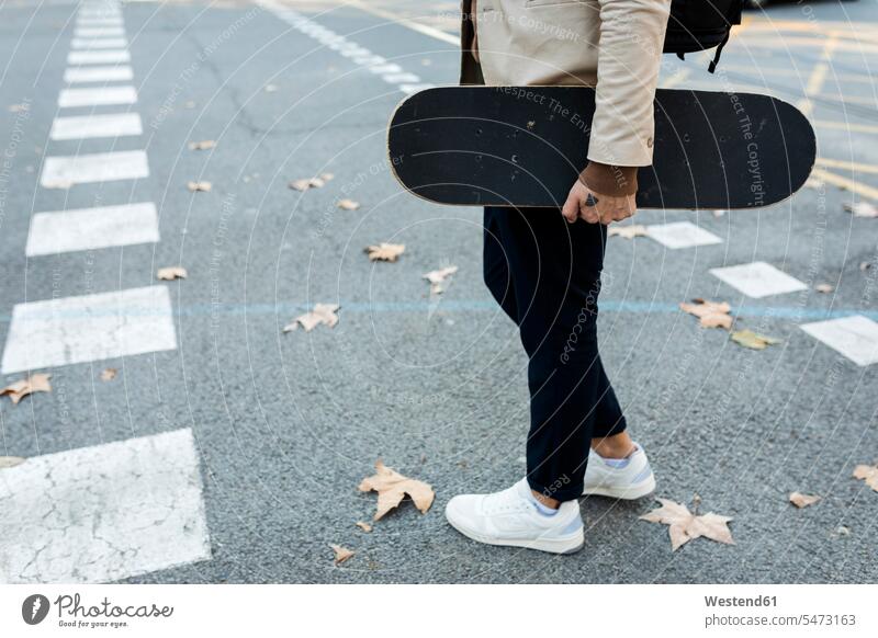 Mann mit Rucksack und Skateboard beim Überqueren der Straße im Herbst, Teilansicht Männer männlich Rucksäcke Rollbretter Skateboards überqueren Strassen Straßen