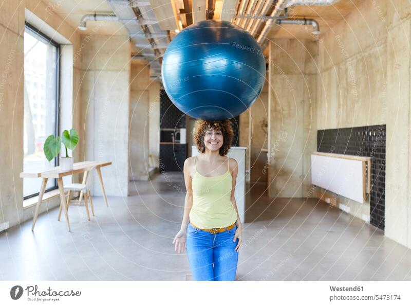 Porträt einer lächelnden Frau, die einen Fitnessball auf ihrem Kopf balanciert unangepasst Unangepasstheit Deutschland Pausenraum Geschäftsfrau Geschäftsfrauen