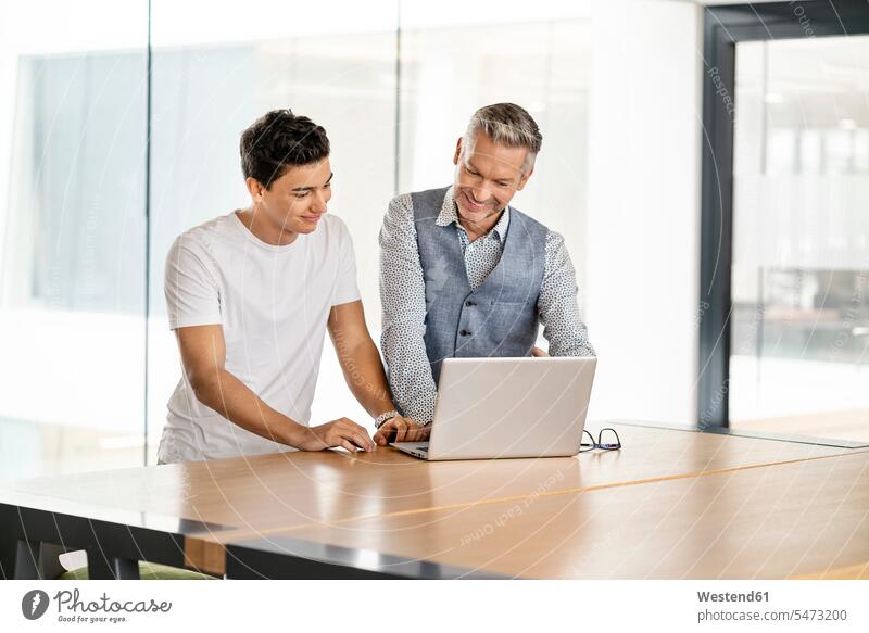 Ein älterer Geschäftsmann arbeitet mit einem jungen Kollegen zusammen und benutzt einen Laptop Europäer zwei Personen junger Mann 20-25 Jahre reifer Mann