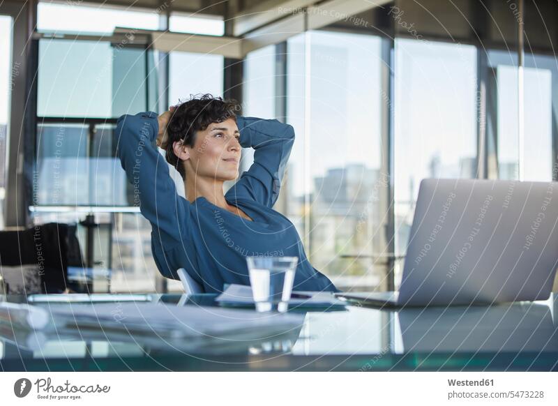 Lächelnde Geschäftsfrau sitzt am Schreibtisch im Büro mit Laptop und macht eine Pause Geschäftsfrauen Businesswomen Businessfrauen Businesswoman lächeln sitzen