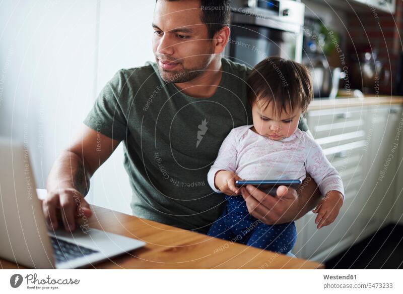 Vater verwendet Laptop mit Baby Mädchen mit Smartphone zu Hause Notebook Laptops Notebooks Tochter Töchter Papas Väter Vati Vatis Papis Zuhause daheim Babies