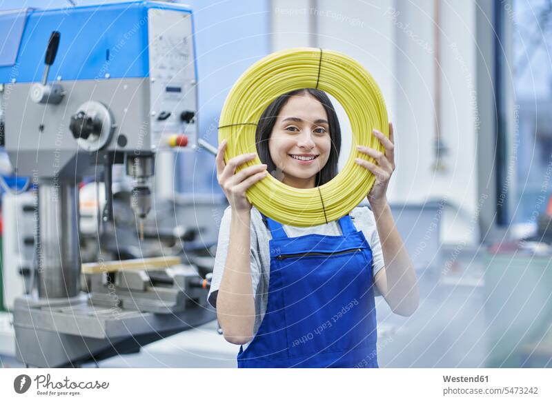Glückliche Arbeitnehmerin schaut durch aufgerollte Kabel in der Fabrik Farbaufnahme Farbe Farbfoto Farbphoto Innenaufnahme Innenaufnahmen innen drinnen Tag