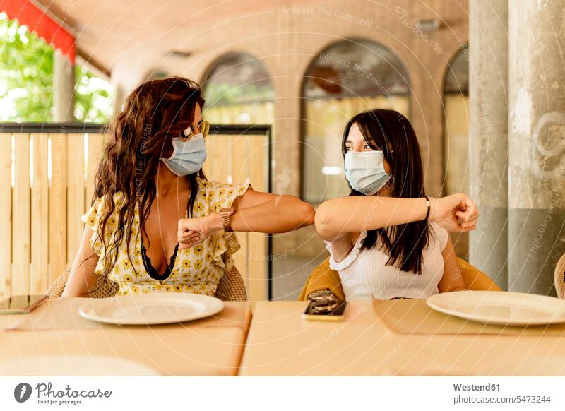 Junge Frauen mit Masken bei der Begrüßung mit Ellbogenbeulen im Restaurant Farbaufnahme Farbe Farbfoto Farbphoto Spanien Innenaufnahme Innenaufnahmen innen