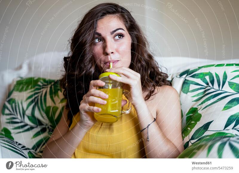 Schöne junge Frau mit langen braunen Haaren trinkt Saft aus Stroh in einem Maurerglas, während sie wegschaut Farbaufnahme Farbe Farbfoto Farbphoto Spanien