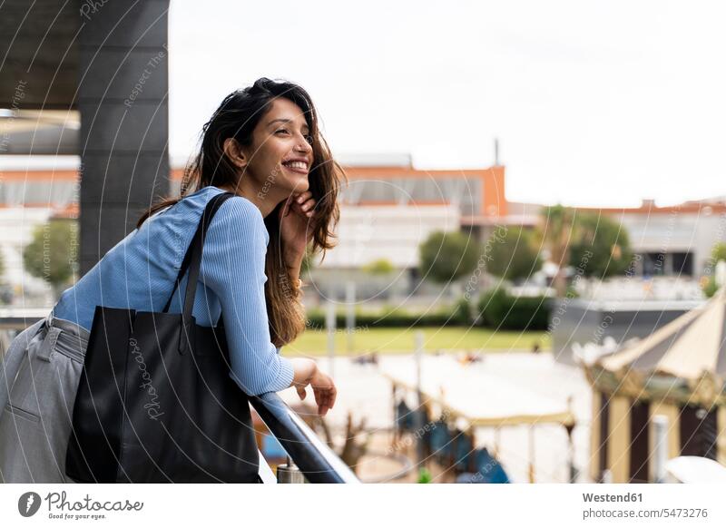 Lächelnde Frau mit an die Reling gelehntem Portemonnaie in der Stadt Farbaufnahme Farbe Farbfoto Farbphoto Außenaufnahme außen draußen im Freien Tag