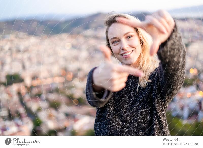 Porträt einer jungen Frau, die bei Sonnenaufgang über der Stadt einen Fingerrahmen macht, Barcelona, Spanien Leute Menschen People Person Personen Europäisch