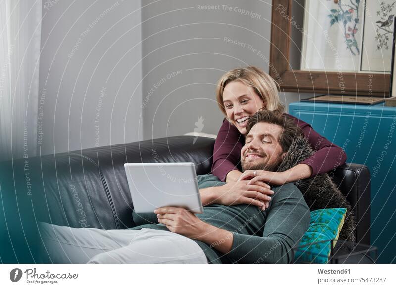 Glückliches Paar mit Tablet auf der Couch zu Hause Sofa Couches Liege Sofas Tablet Computer Tablet-PC Tablet PC iPad Tablet-Computer Pärchen Paare Partnerschaft