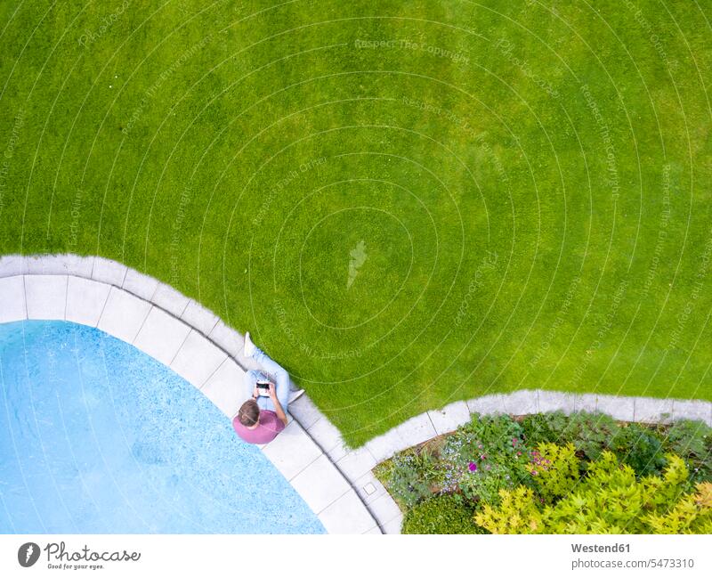 Am Pool sitzender Mann mit ferngesteuerter Navigationsdrohne steuern Männer männlich Beckenrand Drohne Drohnen Swimmingpool Swimmingpools Schwimmbecken