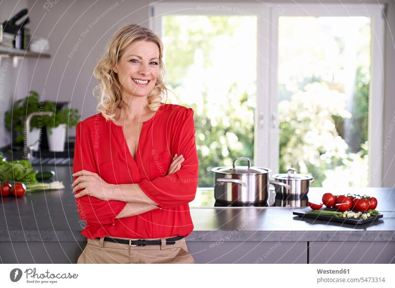 Porträt einer lächelnden Frau in roter Bluse in der Küche stehend rotes Blusen Portrait Porträts Portraits steht Küchen weiblich Frauen Farbe Farbtöne Farbtoene