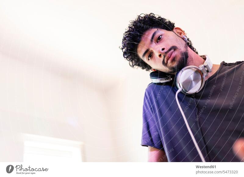 Selbstbewusster junger männlicher DJ, der im Aufnahmestudio über Kopfhörer zuhört Farbaufnahme Farbe Farbfoto Farbphoto Innenaufnahme Innenaufnahmen innen