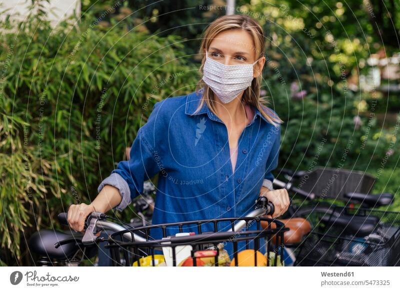 Frau trägt Gesichtsmaske mit Fahrrad und kauft Lebensmittel im Stadtgebiet ein Kleider Raeder Räder Bike Bikes Fahrräder Rad Gesund geschützt schützen außen