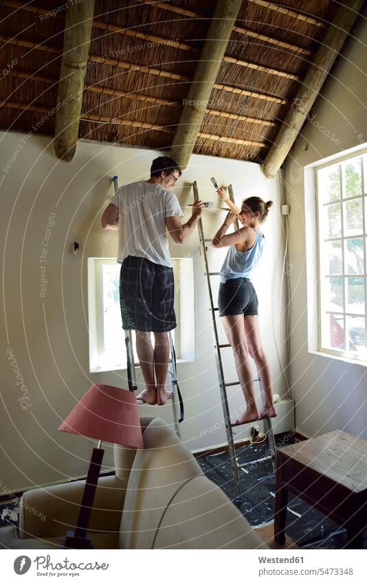 Junges Paar renoviert sein Haus und streicht gemeinsam die Wand Gemeinsam Zusammen Miteinander Zuhause zu Hause daheim streichen renovieren Renovierung Wände
