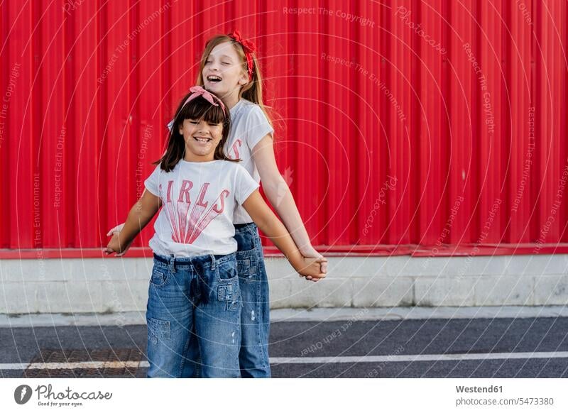Schwestern stehen vor einer roten Wand Hosen Jeanshose T-Shirts freuen geniessen Genuss Glück glücklich sein glücklichsein gefühlvoll Emotionen Empfindung