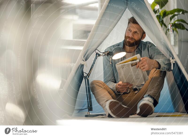 Mann zeltet in seinem Wohnzimmer und liest die Zeitung Allein alleine einzeln Männer männlich Zuhause zu Hause daheim Zeitungen Zelt Zelte lesen Lektüre