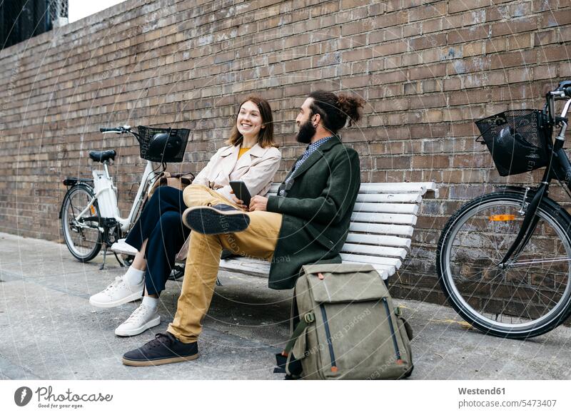 Pärchen sitzt auf einer Bank neben E-Bikes und unterhält sich sitzen sitzend eBikes Elektrofahrrad Elektrorad Paar Paare Partnerschaft Fahrrad Fahrräder Räder