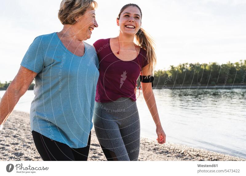 Fit Großmutter und Enkelin zu Fuß am Fluss mit den Armen um, Spaß haben Fitness fit Gesundheit gesund Spass Späße spassig Spässe spaßig Gemeinsam Zusammen