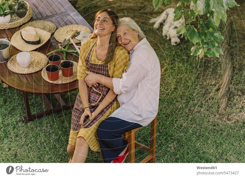 Glückliche Mutter umarmt Tochter, während sie im Hof am Tisch sitzt Farbaufnahme Farbe Farbfoto Farbphoto Spanien Freizeitbeschäftigung Muße Zeit Zeit haben
