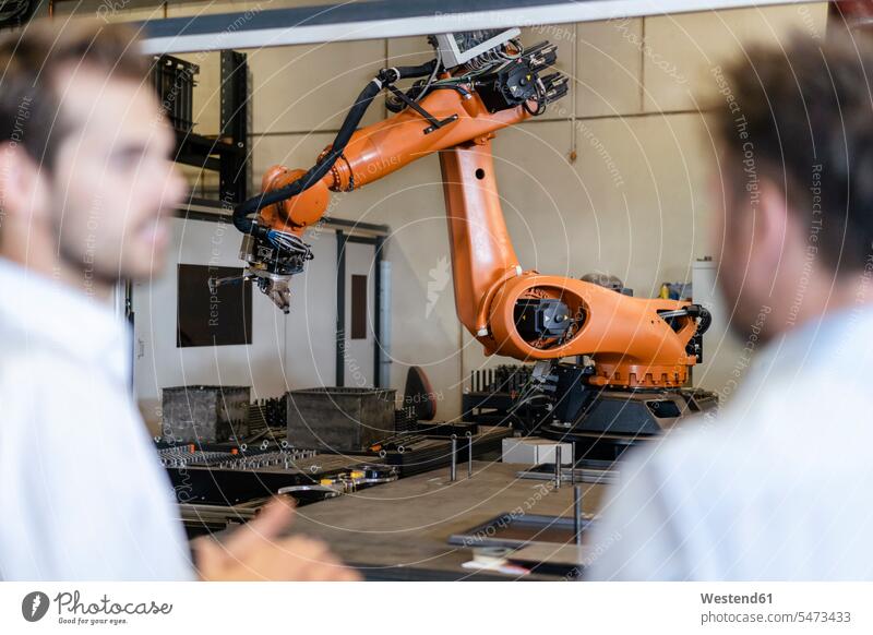 Geschäftsleute stehen gegen automatisierte Roboterarm-Maschine in moderner Fabrik Farbaufnahme Farbe Farbfoto Farbphoto Innenaufnahme Innenaufnahmen innen