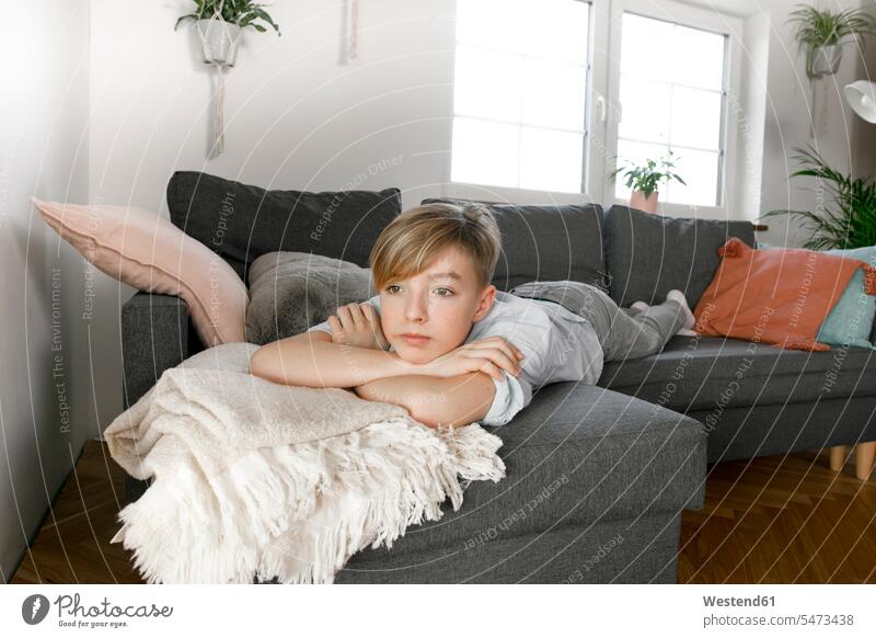 Jugendlicher auf Couch liegend, gelangweilt aussehend langweilig daheim zu Hause Raum Räume Wohnen Wohnraum Wohnräume Wohnung Wohnungen drinnen Innenaufnahmen