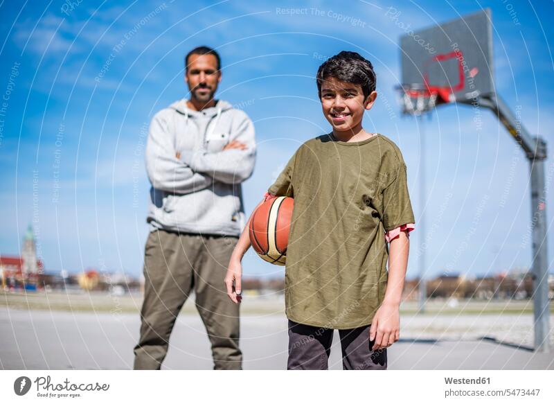 Porträt eines Jungen mit Vater auf einem Basketballplatz im Freien Portrait Porträts Portraits Basketbaelle Basketbälle Papas Väter Vati Vatis Papis Sohn Söhne