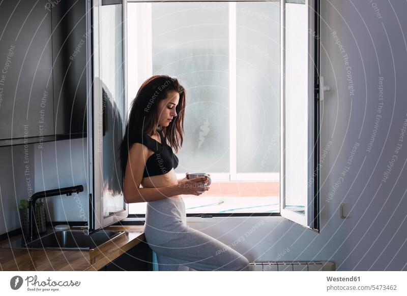Serious schöne junge Frau mit Tasse Kaffee am Fenster zu Hause weiblich Frauen Zuhause daheim Kaffeetasse Kaffeetassen ernst Ernst Ernsthaftigkeit ernsthaft