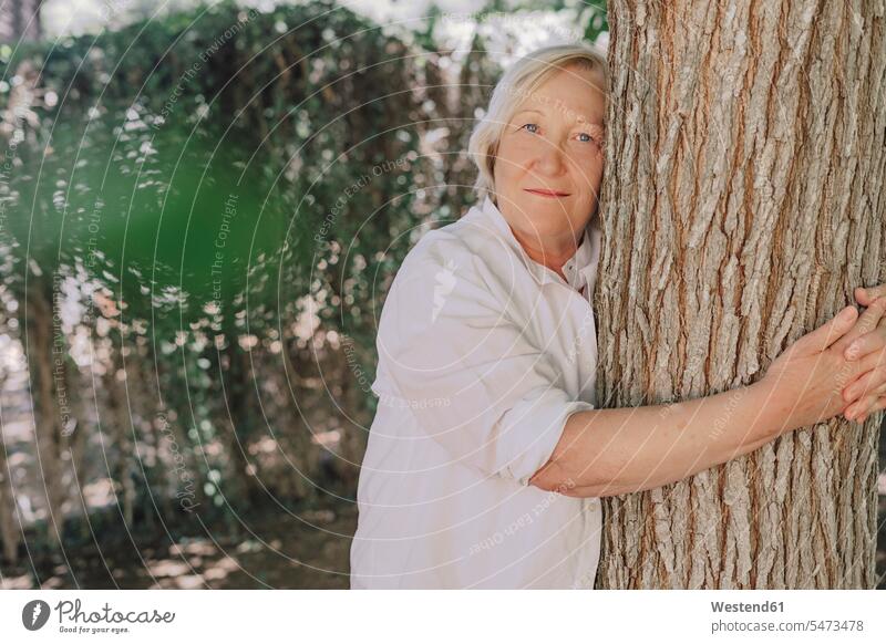 Ältere Frau umarmt Baumstamm, während sie im Hof steht Farbaufnahme Farbe Farbfoto Farbphoto Spanien Freizeitbeschäftigung Muße Zeit Zeit haben Freizeitkleidung