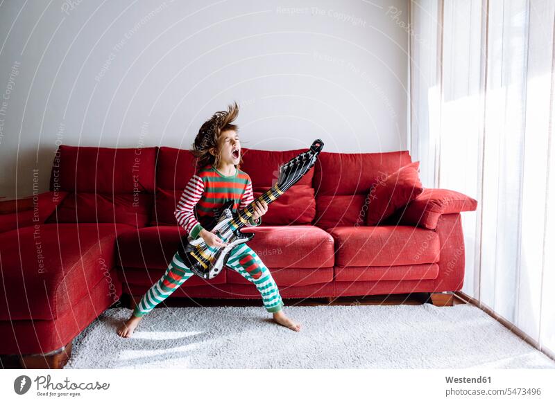Glückliches Mädchen spielt Gitarre gegen Sofa im Wohnzimmer Farbaufnahme Farbe Farbfoto Farbphoto Innenaufnahme Innenaufnahmen innen drinnen Tag
