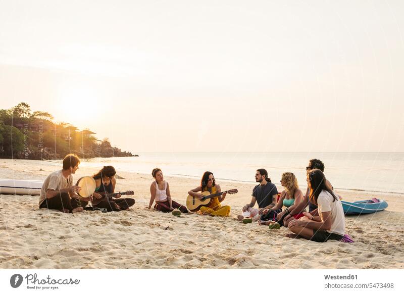 Thailand, Koh Phangan, Gruppe von Menschen, die bei Sonnenuntergang mit Gitarre am Strand sitzen Gitarren sitzend sitzt Menschengruppe Beach Straende Strände