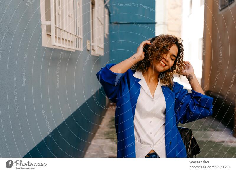 Porträt einer lächelnden Frau, die mit Kopfhörern Musik hört Taschen Jacken Kopfhoerer hoeren freuen geniessen Genuss Glück glücklich sein glücklichsein blaue