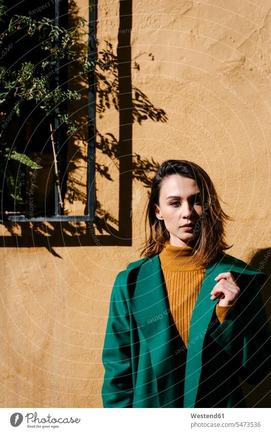 Schöne Frau in grüner Jacke steht an sonnigen Tagen an der Wand Farbaufnahme Farbe Farbfoto Farbphoto Spanien Freizeitkleidung Freizeitbekleidung casual