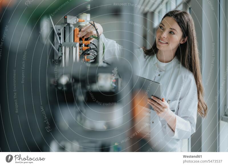 Lächelnde Wissenschaftlerin hält digitale Tablette in der Hand und erfindet Maschine im Labor Farbaufnahme Farbe Farbfoto Farbphoto Innenaufnahme Innenaufnahmen