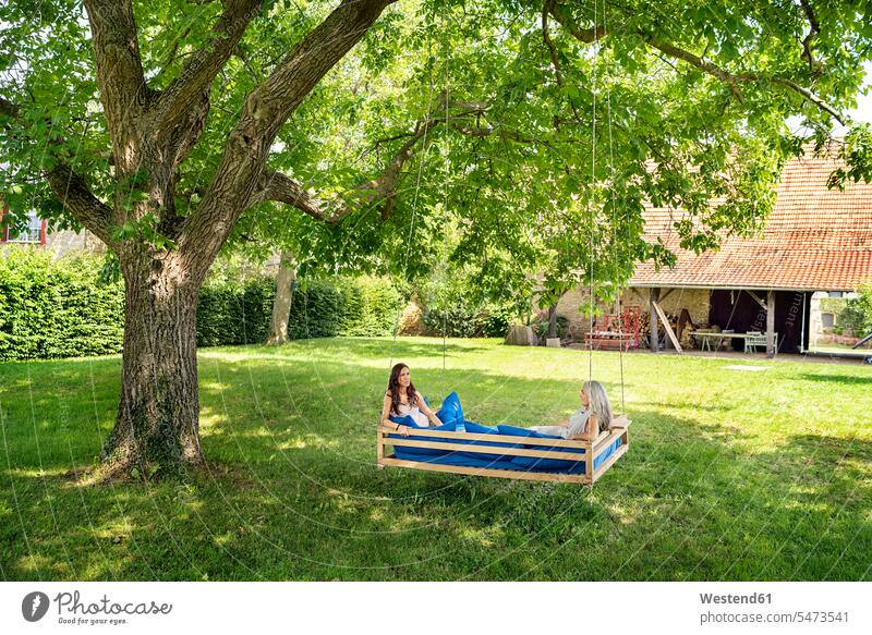 Zwei Frauen entspannen auf einem Hängebett im Garten hängen Bett Betten entspannt entspanntheit relaxt Freundinnen Hängematte Hängematten weiblich Gärten