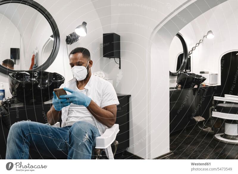 Barbier trägt chirurgische Maske und Handschuhe mit Smartphone Job Berufe Berufstätigkeit Beschäftigung Jobs Telekommunikation telefonieren Handies Handys