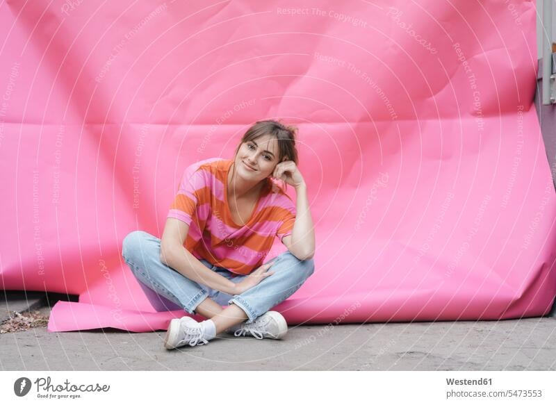 Selbstbewusste junge Frau sitzt auf rosa Hintergrund Unbeschwert Sorglos sitzen sitzend glücklich Glück glücklich sein glücklichsein pink pinkfarben weiblich