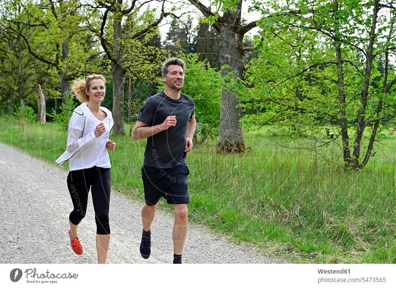 Paar rennt auf Feldweg gegen Bäume im Wald Farbaufnahme Farbe Farbfoto Farbphoto Deutschland Wälder Forst Natur Außenaufnahme außen draußen im Freien Tag