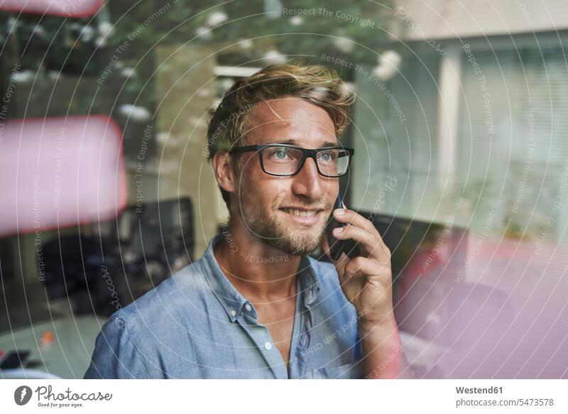 Lässiger junger Geschäftsmann am Telefon hinter einer Fensterscheibe im Büro geschäftlich Geschäftsleben Geschäftswelt Geschäftsperson Geschäftspersonen