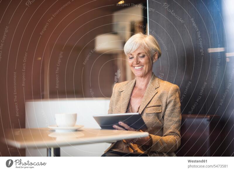 Lächelnde ältere Geschäftsfrau mit Tablet in einem Café Geschäftsfrauen Businesswomen Businessfrauen Businesswoman Cafe Kaffeehaus Bistro Cafes Cafés